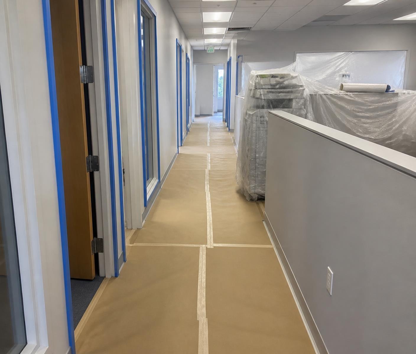 Office hallway prepped with taped floor paper, plastic over furniture and blue tape on frames