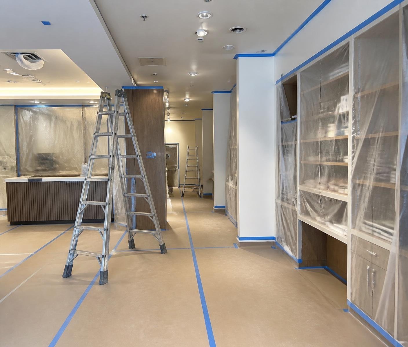 Commercial interior fully masked with plastic over shelving, taped floor paper and ladders