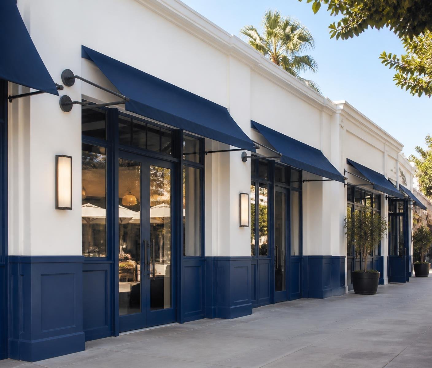 Row of retail storefronts painted white with deep blue trim, awnings and wall sconces