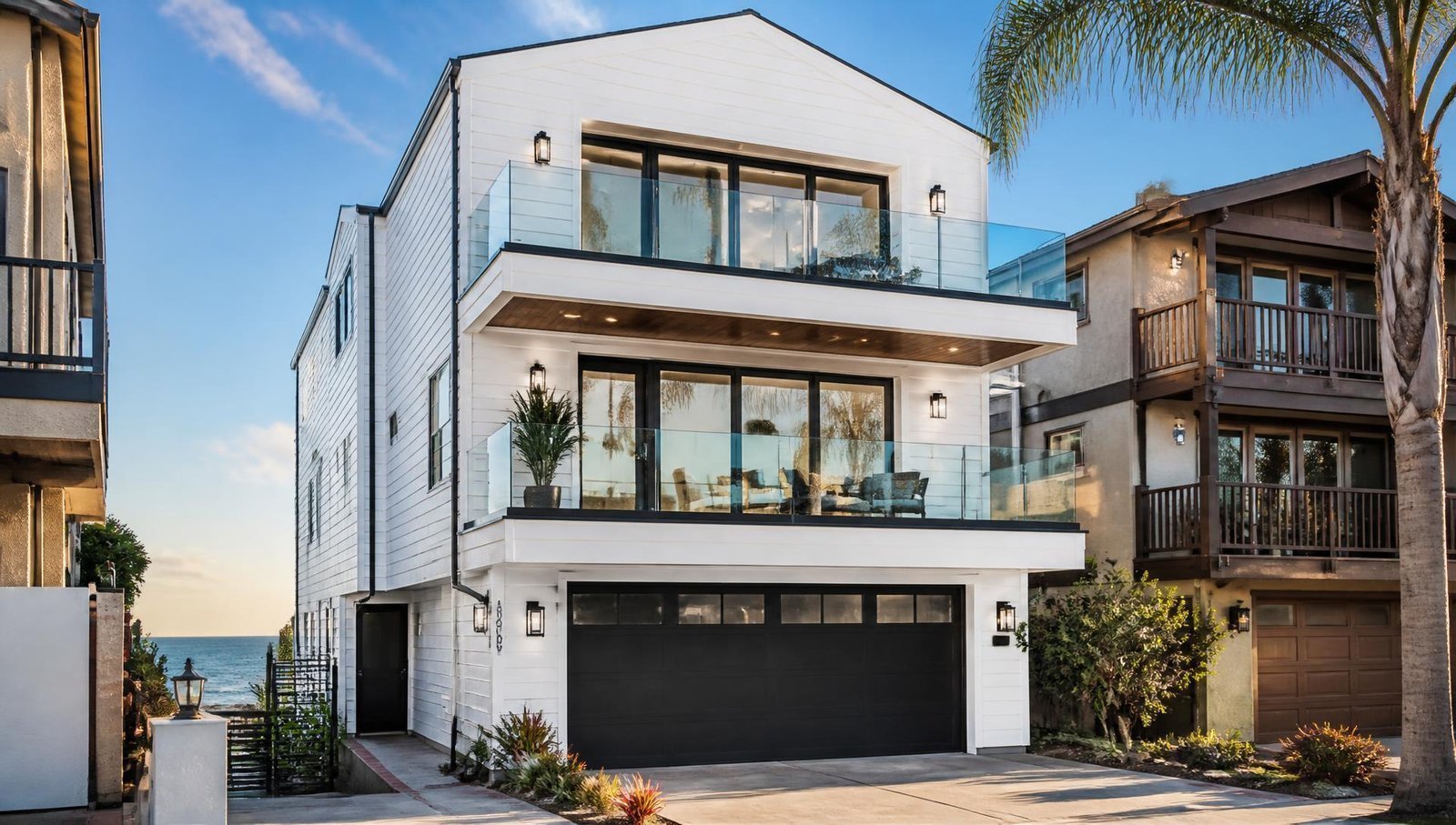 Three story Manhattan Beach home with fresh white siding, dark trim, and glass railings