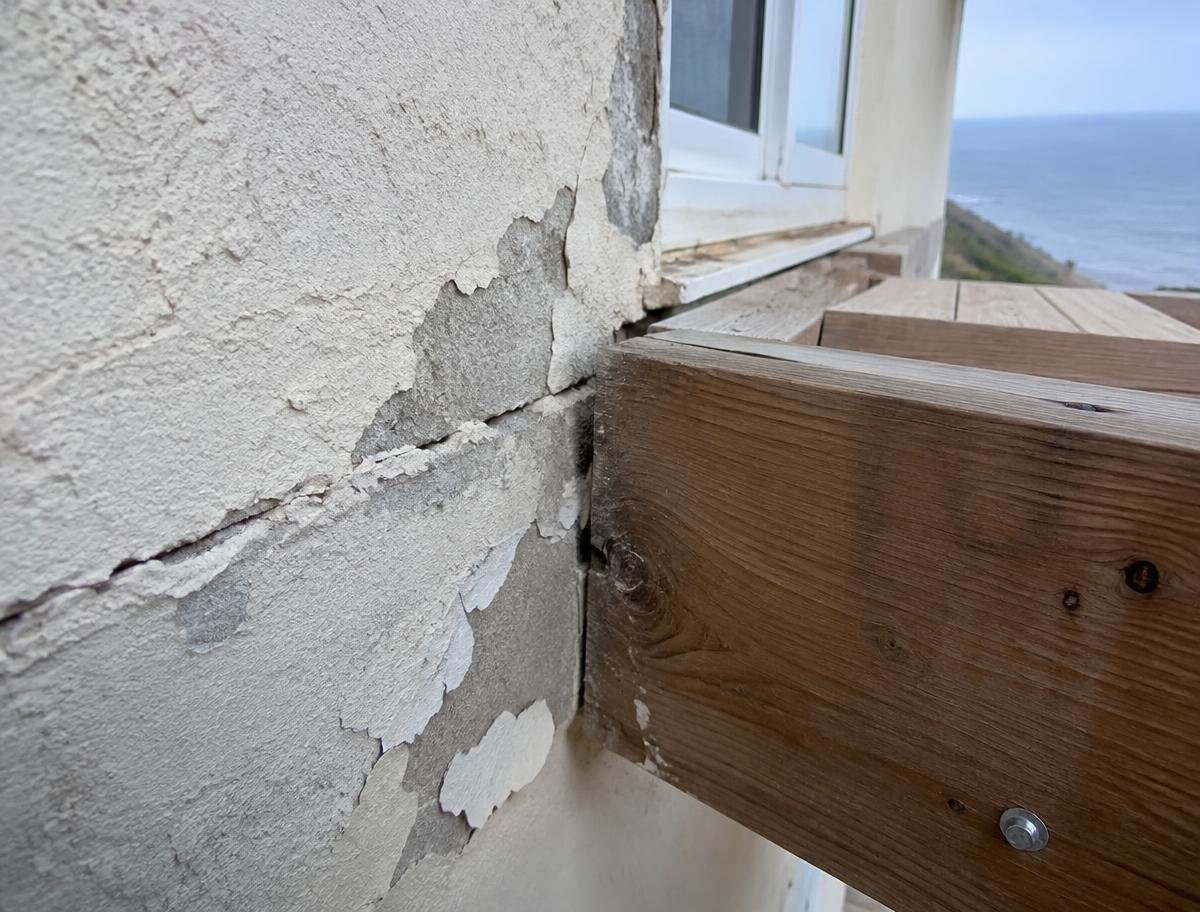 Cracked stucco and peeling paint where a deck ledger meets the house