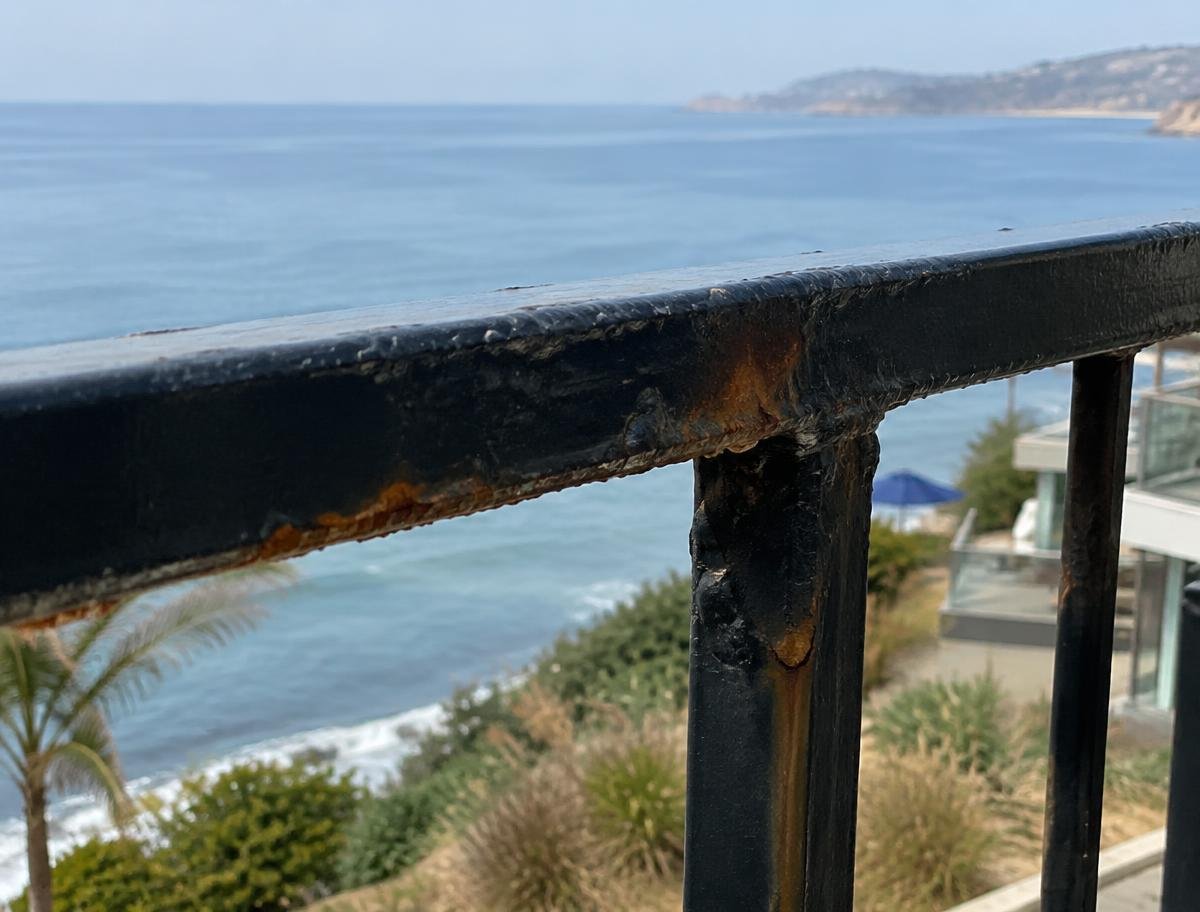 Rust bleeding through black paint on a balcony railing above the ocean